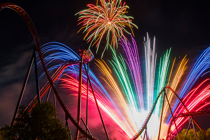 A thrilling roller coaster ride at Canada’s Wonderland amusement park with a fireworks display in the background
